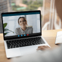 A person participates in a video call with a woman on their laptop screen, displayed in an office setting